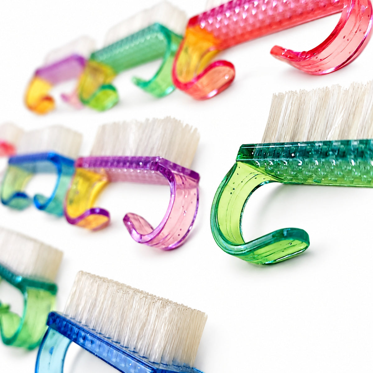 Brosses de nettoyage pour ongles avec poignées transparentes colorées et poils blancs.