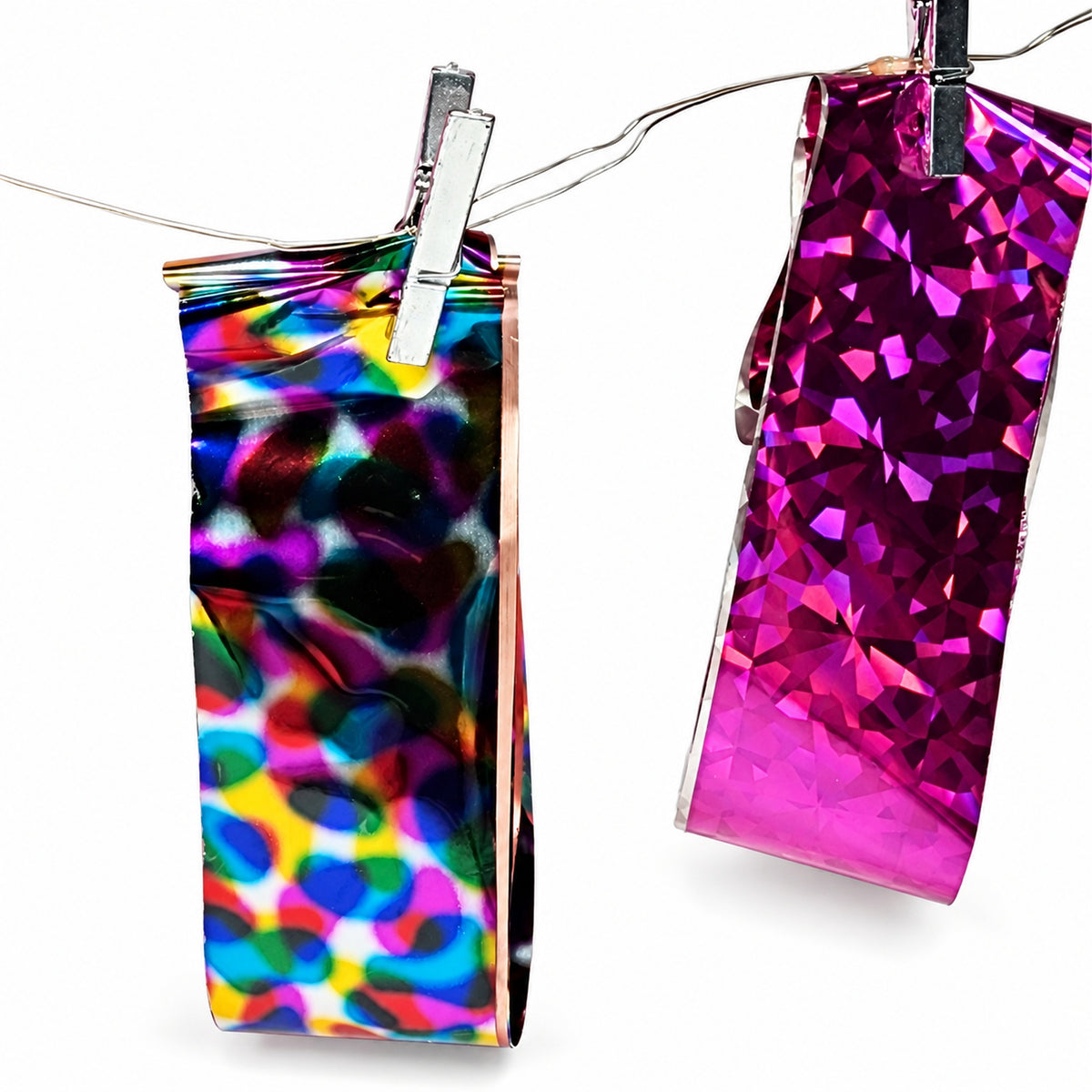 Feuilles de foil holographique à motifs multicolores et fuchsia suspendues par des pinces.